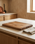 Thick acacia wood serving board with juice groove, bare on a stone worktop