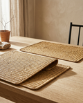 Rectangular woven seagrass placemats, bare, laid on a white oak dining table