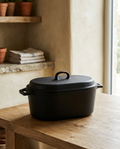 Enamelled cast iron casserole pot with dual handles, lid on and empty, on a white oak worktop
