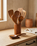 9 piece teak wooden kitchen utensil set standing in its holder on a white oak worktop